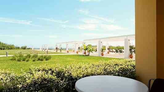 Udsigt fra en terrasse med et rundt bord mod en græsplæne og pergola i baggrunden. (AI-genereret tekst)