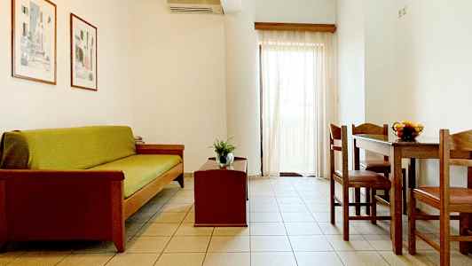 En stue med sofa, sofabord og spisebord med stole. Lyse vægge og gardiner. (AI-genereret tekst)