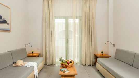 En stue med to grå sofaer, et bord med frugtkurv og en bog samt gardiner foran vinduet. (AI-genereret tekst)