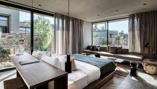 Billede af et moderne hotelværelse med stor seng, skrivebord og sofa samt vinduer med udsigt til en frodig gårdhave. (AI-genereret tekst)