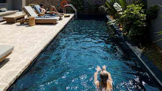 Person svømmer i en pool med liggestole ved siden af. (AI-genereret tekst)