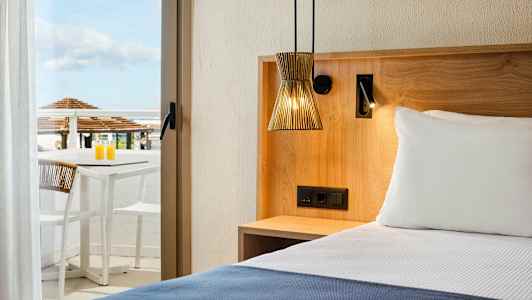 Hotelværelse med en seng, træinteriør og en terrasse med bord og stole i baggrunden. (AI-genereret tekst)