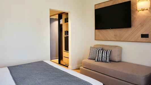 Et hotelværelse med en seng, en sofa, et vægmonteret TV og et åbent klædeskab. (AI-genereret tekst)