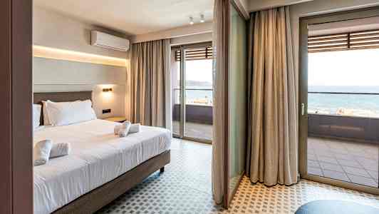 Hotelværelse med seng og håndklæder, store glasdøre der fører ud til en balkon med havudsigt. (AI-genereret tekst)