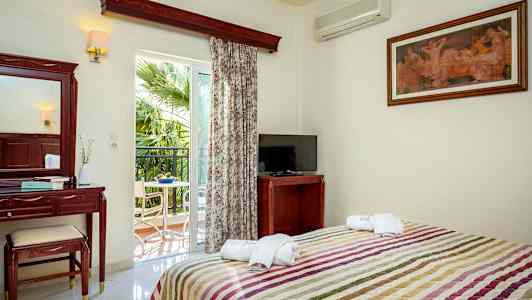 Et hotelværelse med seng, TV, makeupbord og altan med udsigt til en palme. (AI-genereret tekst)