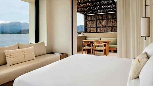 Et hotelværelse med udsigt over bjerge og hav samt en terrasse med siddeområde. (AI-genereret tekst)