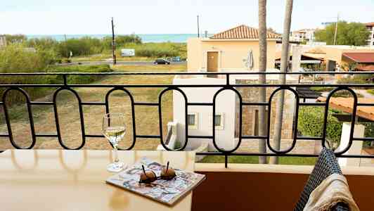 Altan med bord, vinglas og blad, udsigt over græsplæne og hav. (AI-genereret tekst)