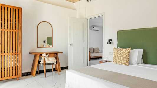 Et soveværelse med en grøn sengegavl, et skrivebord af træ med et spejl ovenover og et trædetaljeret garderobeskab. (AI-genereret tekst)