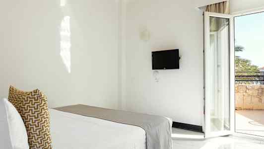 Et hotelværelse med en seng, en vægmonteret TV og en altandør. (AI-genereret tekst)