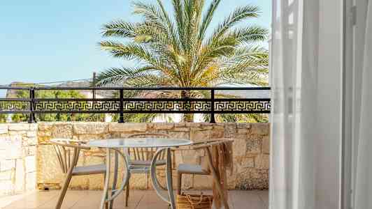 Udsigt over en solrig terrasse med bord og stole, mod en palme og blå himmel. (AI-genereret tekst)