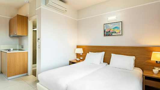 Hotelværelse med to senge, natbord og et lille tekøkken. (AI-genereret tekst)