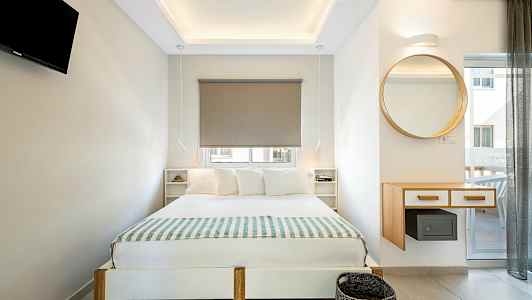 Moderne indrettet soveværelse med dobbeltseng, vægmonteret TV og et rundt spejl. (AI-genereret tekst)