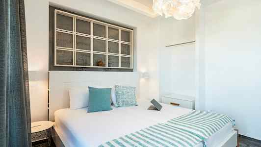 Et lyst og moderne hotelværelse med en dobbeltseng, sengelamper, hvide vægge og dekorative detaljer. (AI-genereret tekst)