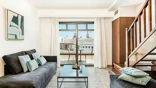 En stue med en sofa, et bord og en trappe, samt en balkon med udsigt. (AI-genereret tekst)