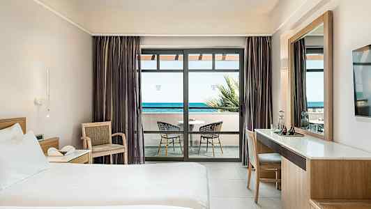 Hotelværelse med seng, skrivebord og altan med havudsigt. (AI-genereret tekst)