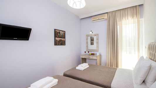 Billede af et værelse med to enkeltsenge, sengelinned og puder, et vægmonteret fjernsyn, et spejl med belysning over et skrivebord og et vindue med lyse gardiner. (AI-genereret tekst)