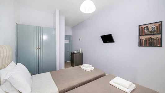 Hotelværelse med to enkeltsenge, et klædeskab, et lille køleskab og et vægmonteret fjernsyn. (AI-genereret tekst)