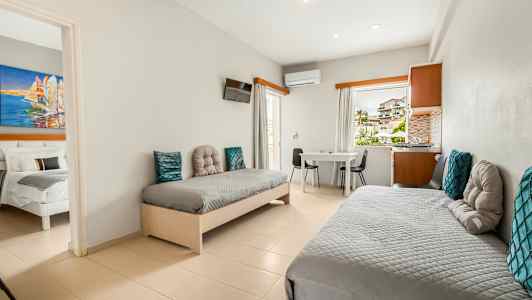 Et hotelværelse med to enkeltsenge, et bord og stole samt udsigt gennem vinduet. (AI-genereret tekst)