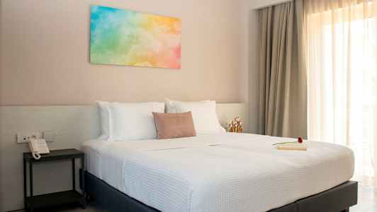 Et soveværelse med en dobbeltseng, hvide sengetøj og et farverigt maleri på væggen. (AI-genereret tekst)