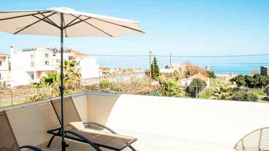 Liggestole og parasol på en terrasse med udsigt over havet og omkringliggende bygninger. (AI-genereret tekst)