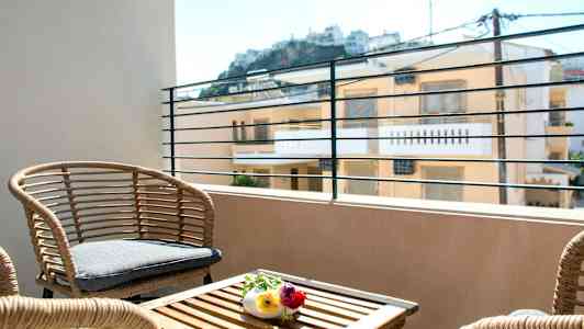 En terrasse med rottingmøbler og udsigt til bygninger i baggrunden. (AI-genereret tekst)