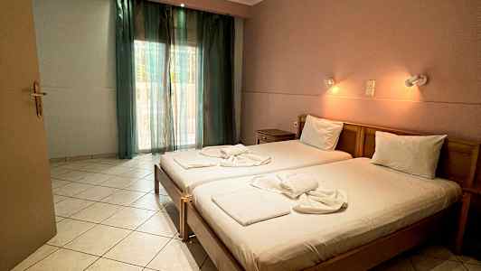 Et hotelværelse med to enkeltsenge, redt og belyst af væglamper, samt et vindue med grønne gardiner. (AI-genereret tekst)