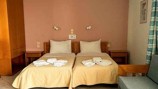 Et hotelværelse med to enkeltsenge, natborde og sammenfoldede håndklæder på sengene. (AI-genereret tekst)