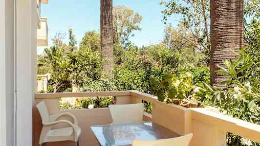 En altan med bord og stole, omgivet af grønne planter og palmer. (AI-genereret tekst)