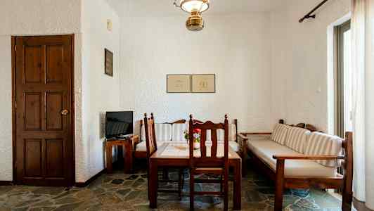 Et rum med et træbord og stole, en sofa samt en dør og et tv på et træbord. (AI-genereret tekst)