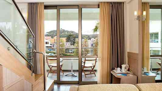 Hotelværelse med en balkon med udsigt over omgivelserne. Trappetrin fører til en højere niveau. En lille siddegruppe er på balkonen. (AI-genereret tekst)