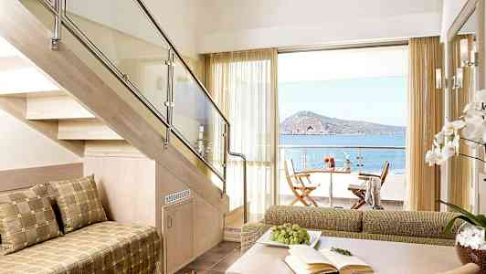 Et moderne rum med en trappe af træ, siddepladser og udsigt over havet fra en terrasse. (AI-genereret tekst)