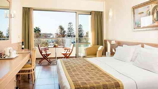 Hotelværelse med dobbeltseng, skrivebord, siddepladser og en balkon med to stole og et bord. (AI-genereret tekst)