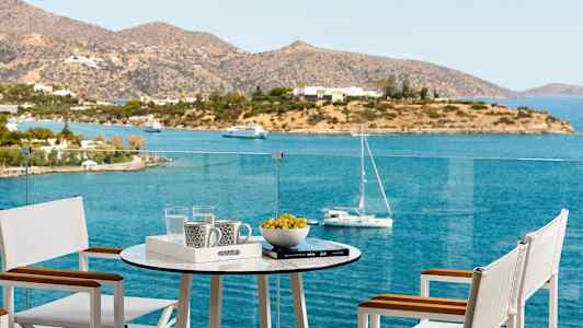 En terrasse med bord og stole med udsigt over havet og en ø. (AI-genereret tekst)