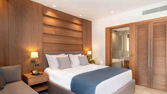 Et hotelværelse med en dobbeltseng, træpaneler på væggen og en skydedør, der fører til badeværelset. (AI-genereret tekst)