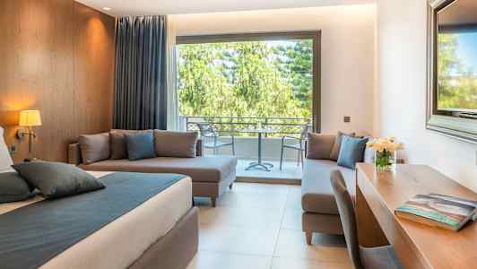 Moderne værelse med seng, skrivebord og siddeområde, udsigt til gårdhave med grønt. (AI-genereret tekst)