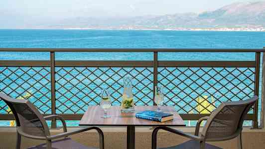 To stole ved et bord med en karaffel og to glas, med udsigt over havet. (AI-genereret tekst)