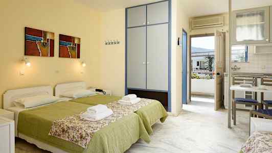 To senge med grønt sengetøj og blomstrede sengeoverkast i et rum med skab, køkkenbord og dør til altan. (AI-genereret tekst)