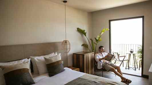 Et hotelværelse med en opredt dobbeltseng, moderne indretning og en altan med havemøbler samt grønne planter. (AI-genereret tekst)