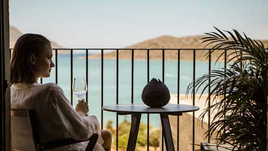 En person sidder på en altan og holder et glas med udsigt over havet. (AI-genereret tekst)