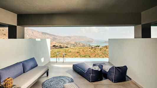 En lounge med siddepladser og udsigt over et landskab og hav. (AI-genereret tekst)