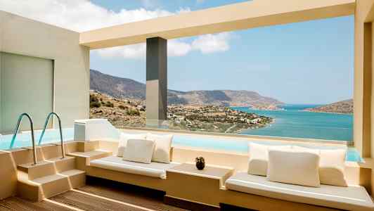 Terrasse med siddepladser ved pool med udsigt over havet og bjerge. (AI-genereret tekst)