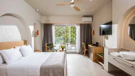 Et hotelværelse med en stor seng, siddepladser, skrivebord og en balkon med udsigt til grønt. (AI-genereret tekst)