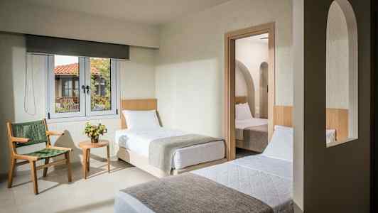 Et hotelværelse med to enkeltsenge, et vindue og en dør til et andet værelse med en seng. (AI-genereret tekst)