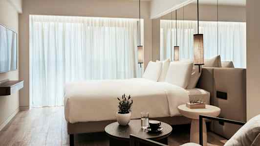 Et moderne hotelværelse med en stor seng, hvide lagner og minimalistisk indretning. (AI-genereret tekst)