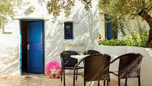 Hvid bygning med blå dør og vinduer, bord og stole på terrasse. (AI-genereret tekst)