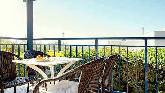 Terrasse med bord og fire rottingstole, udsigt til grønt og blå himmel. (AI-genereret tekst)