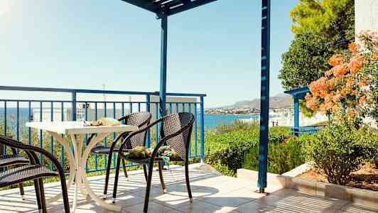 En terrasse med stole og et bord, havudsigt og grønne områder. (AI-genereret tekst)