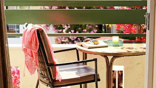 En stol med et lyserødt klæde, et bord med solbriller, en bog og et lys står på en terrasse. (AI-genereret tekst)