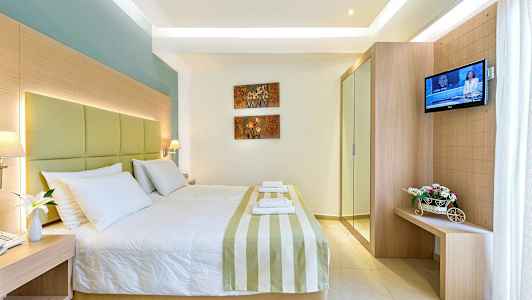 Et hotelværelse med en stor seng, dekoreret med stribet sengetæppe og hvide puder. På væggen er der kunst med blomstermotiver, og til højre er der et fjernsyn samt et lille møbel med blomster. (AI-genereret tekst)