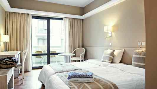 Hotelværelse med to enkeltsenge, skrivebord og altan. (AI-genereret tekst)